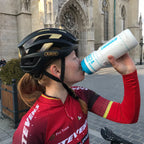 Cyclist in red jersey drinking from a water bottle with a cathedral in the background