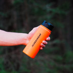 Hand holding an orange bottle labeled 'INCREDIWEAR' against a blurred green background