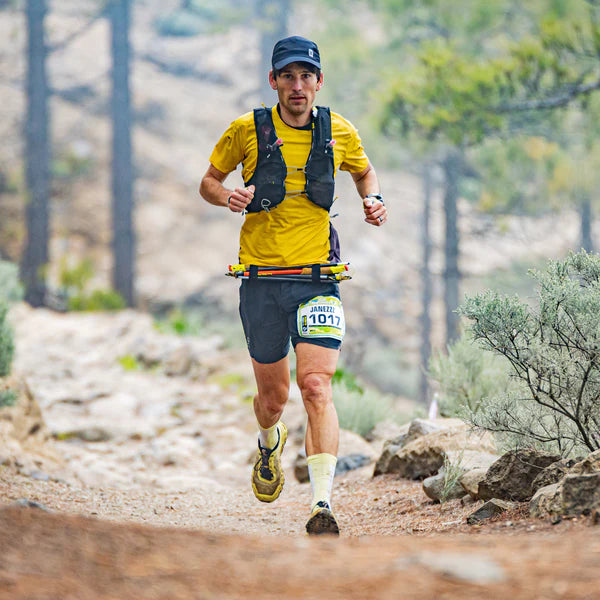 Man running on a trail with a backpack and race number