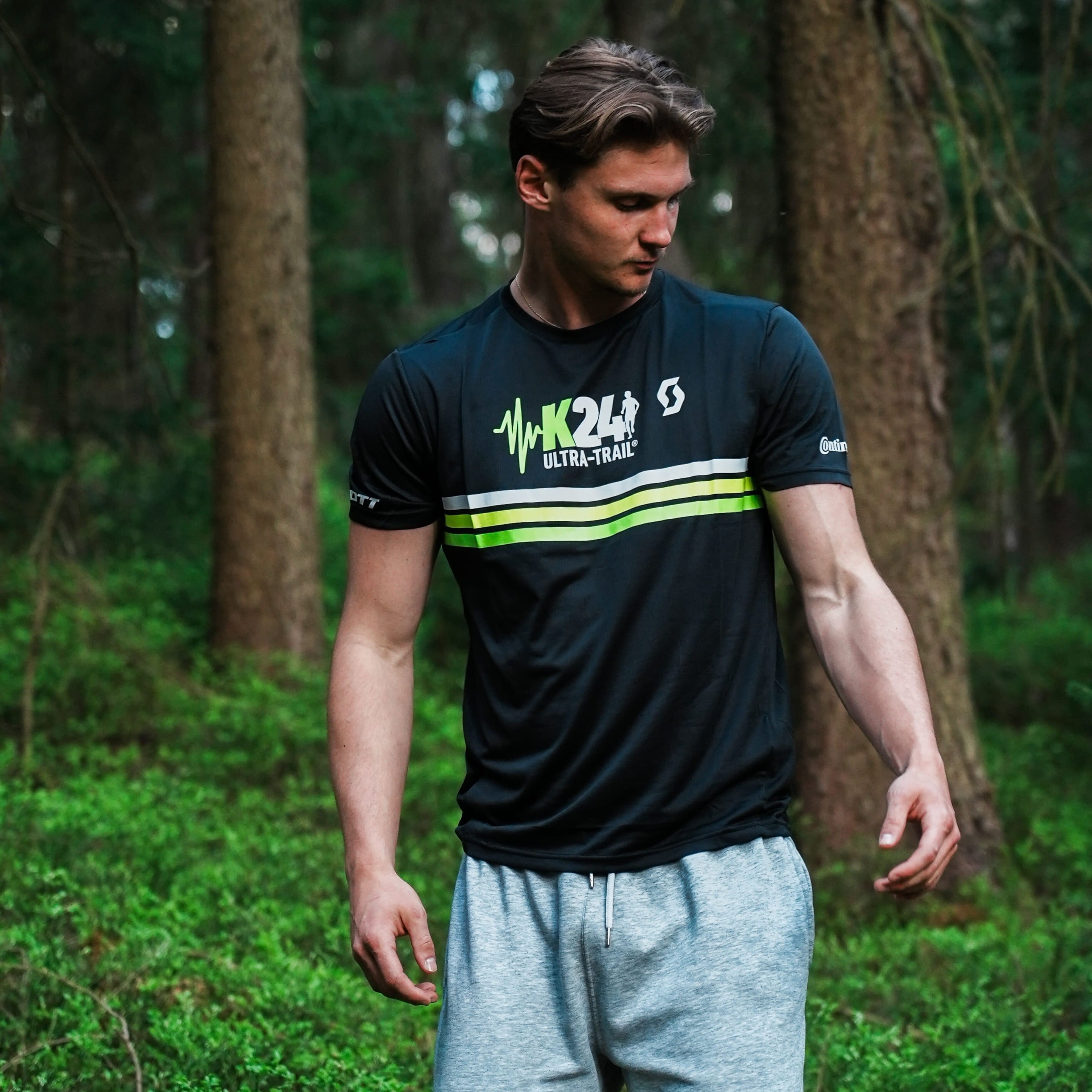Man wearing a black athletic shirt with green and white design in a forest setting