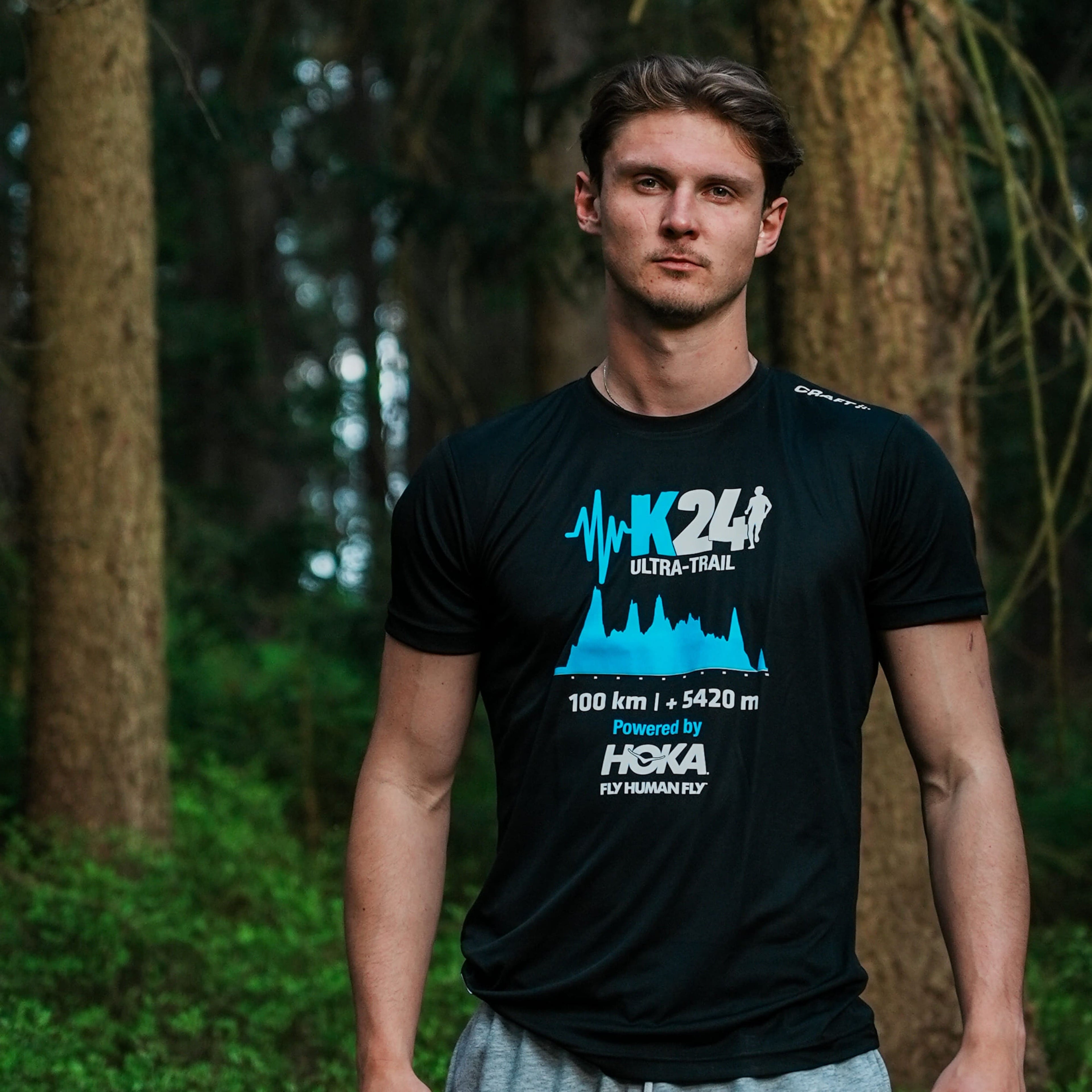 Man wearing a black t-shirt with K24 Ultra-Trail branding in a forest setting