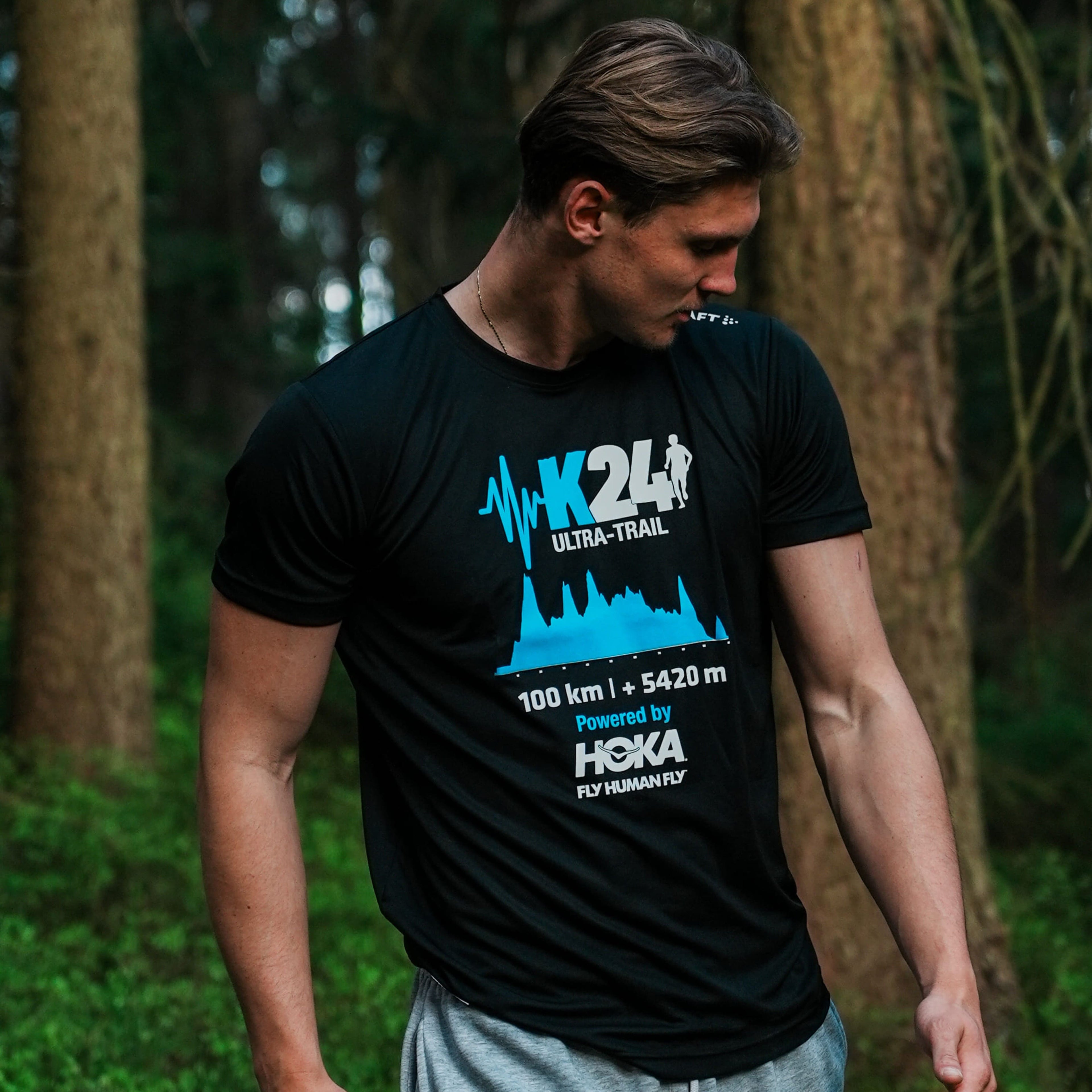 Man wearing a black t-shirt with blue and white graphics in a forest setting