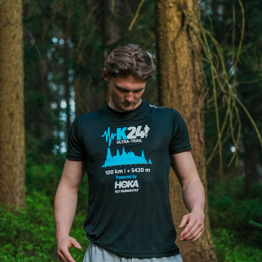 Man wearing a black t-shirt with blue and white text and graphics in a forest setting