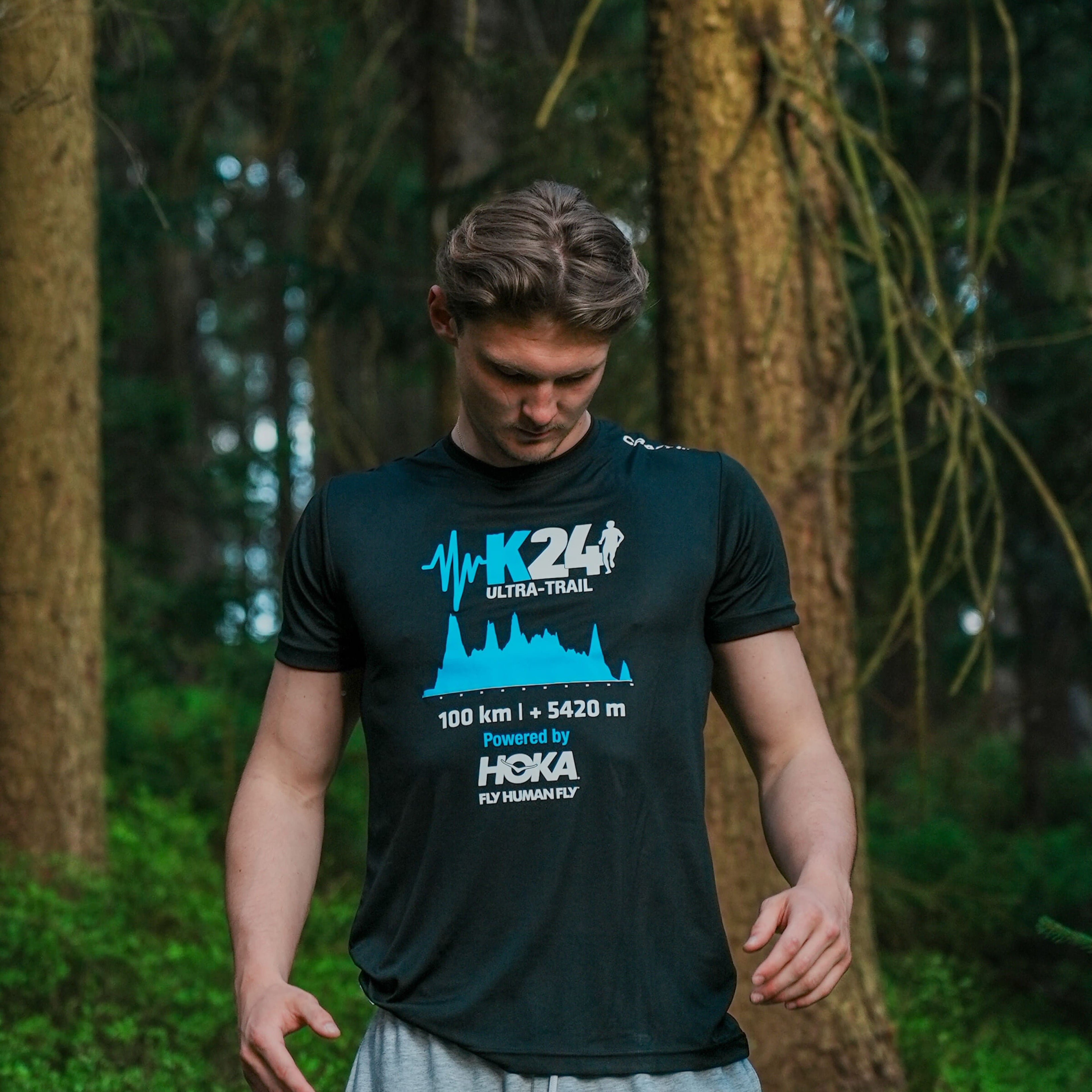 Man wearing a black t-shirt with blue and white text and graphics in a forest setting