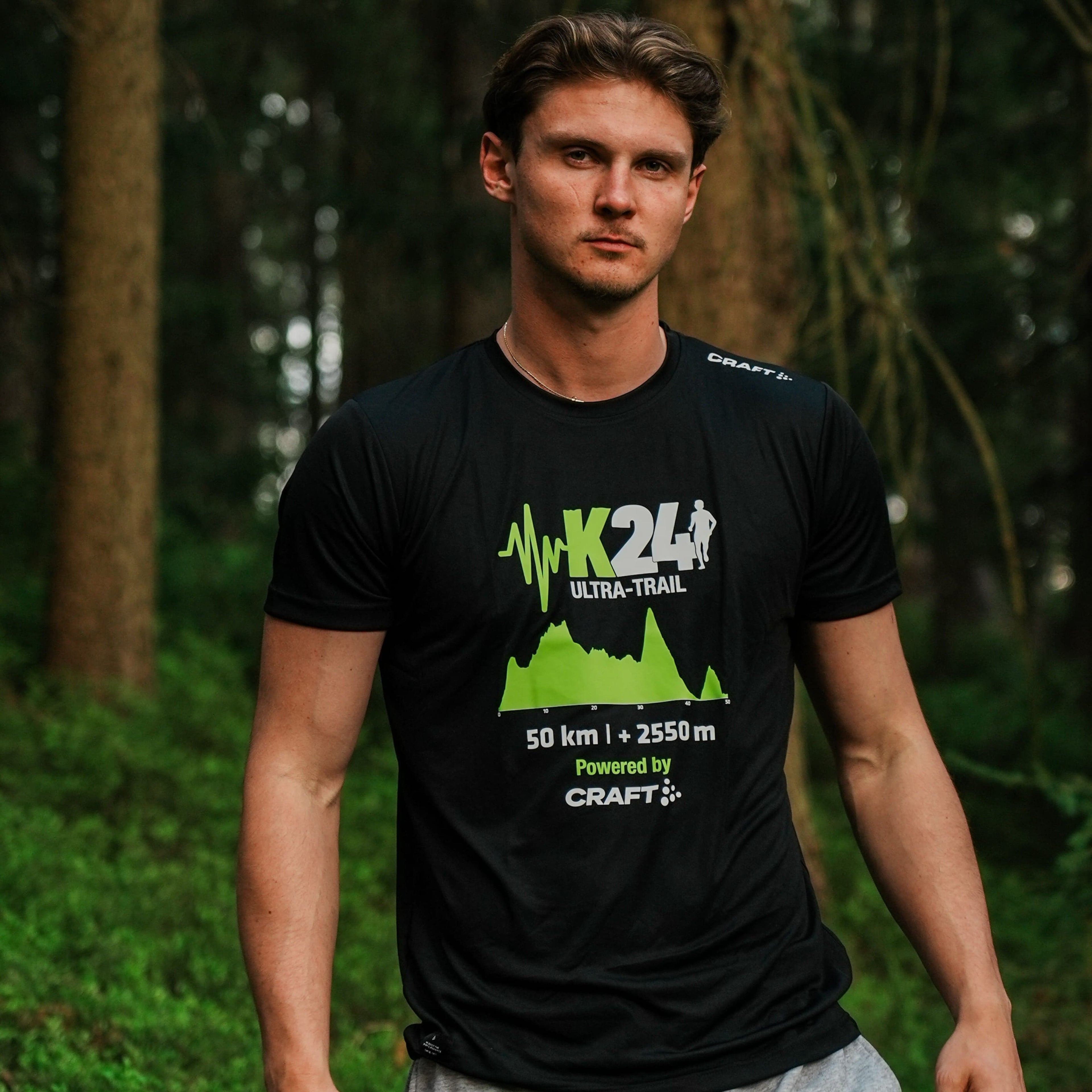 Man wearing a black t-shirt with green and white text and graphics in a forest setting