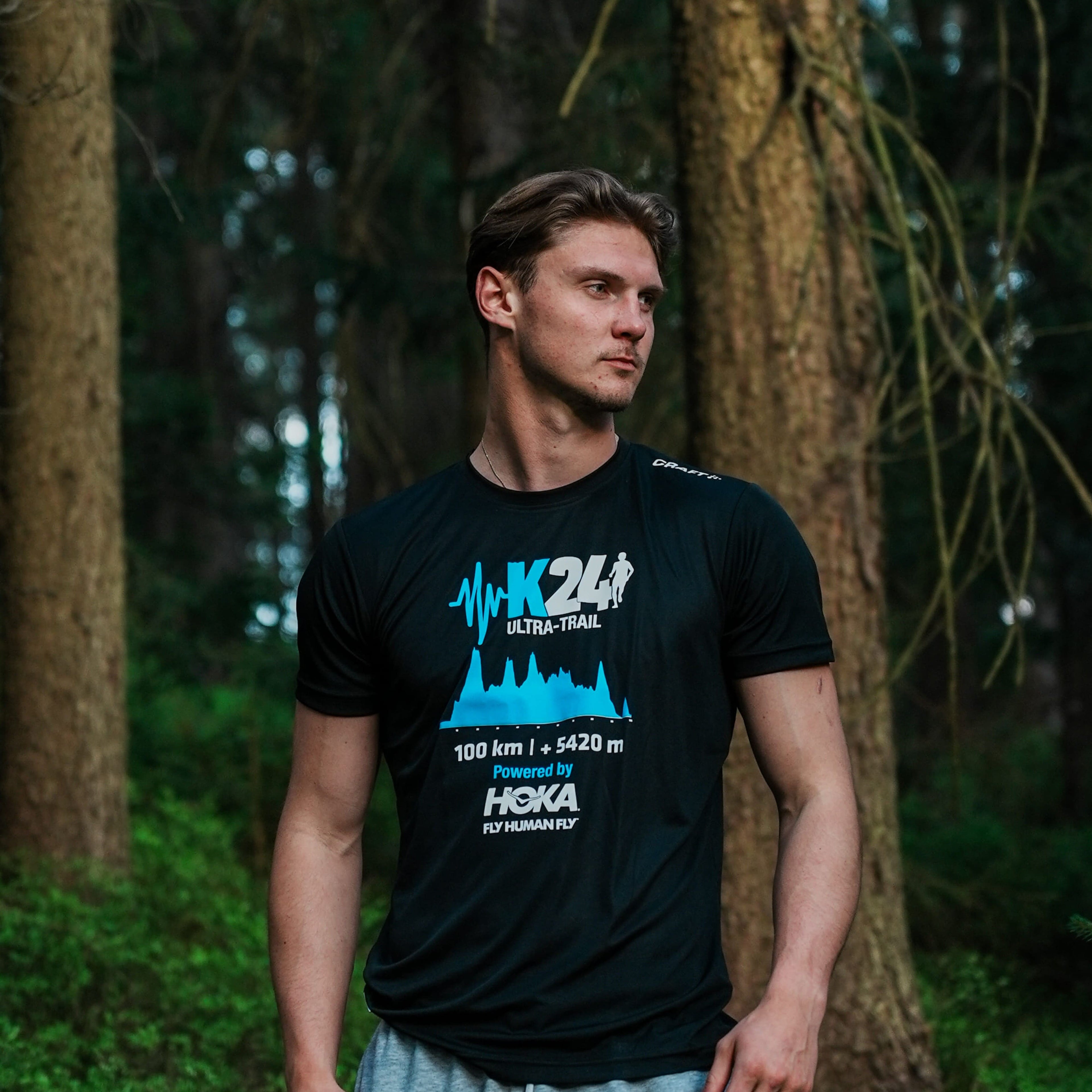 Man wearing a black t-shirt with blue and white graphics in a forest setting