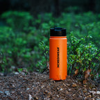 Orange water bottle with black lid on a forest floor