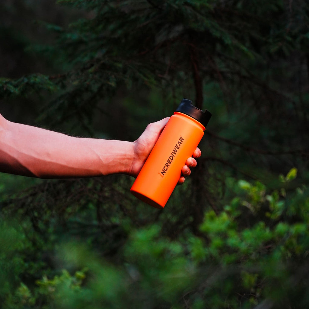 Person holding an orange water bottle with a blurred forest background