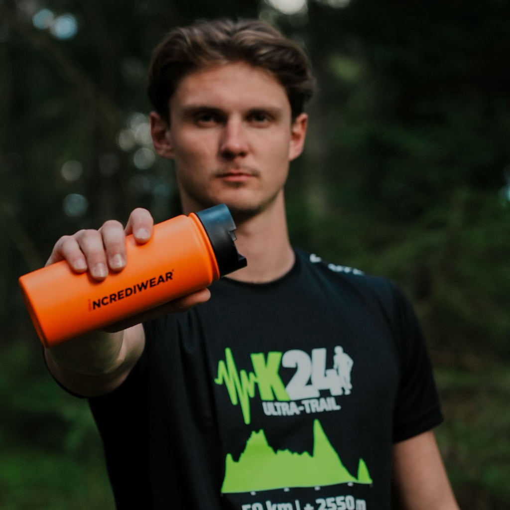 Person holding an orange water bottle with a blurred green background