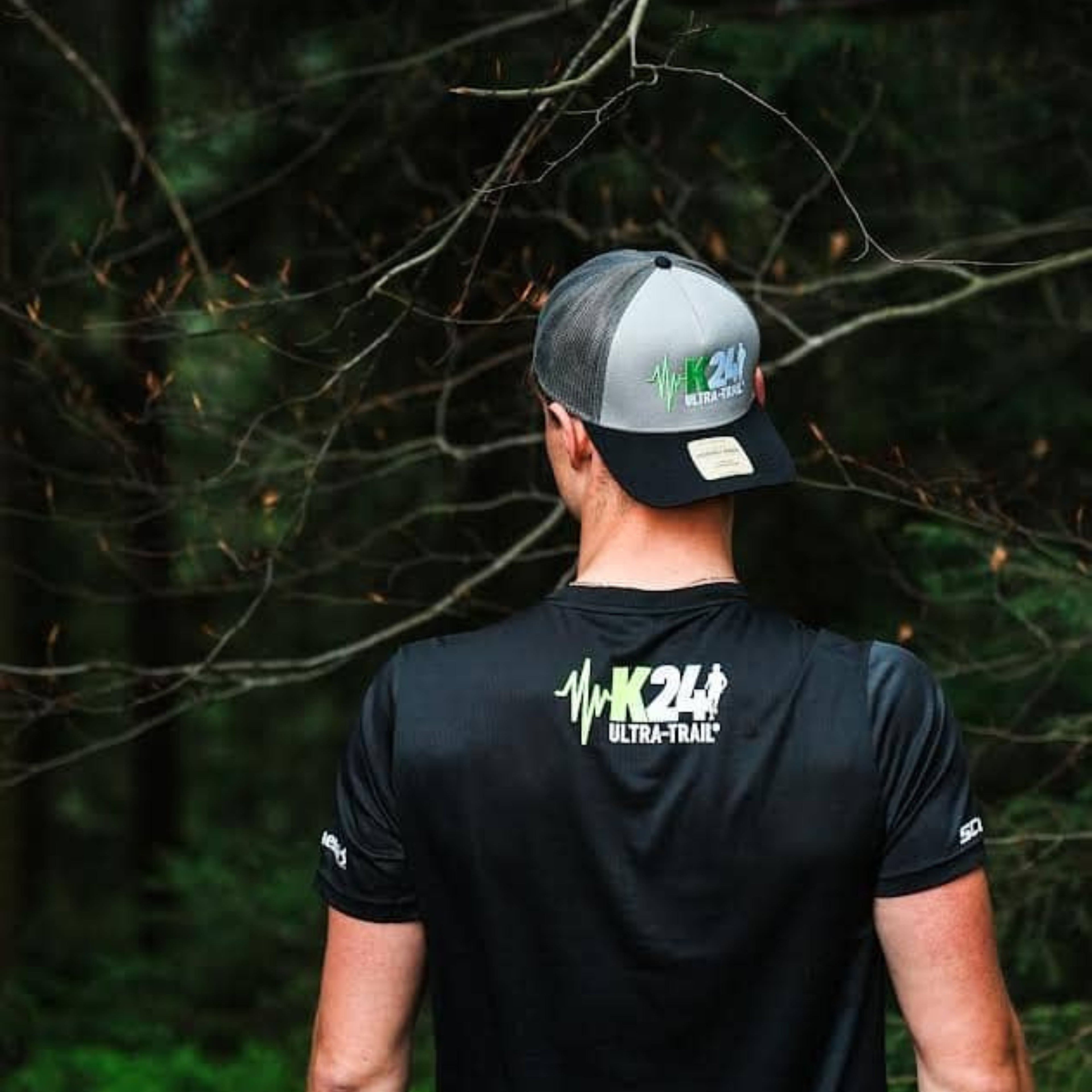 Person wearing a black 'K24 Ultra Trail' shirt and cap in a forest setting