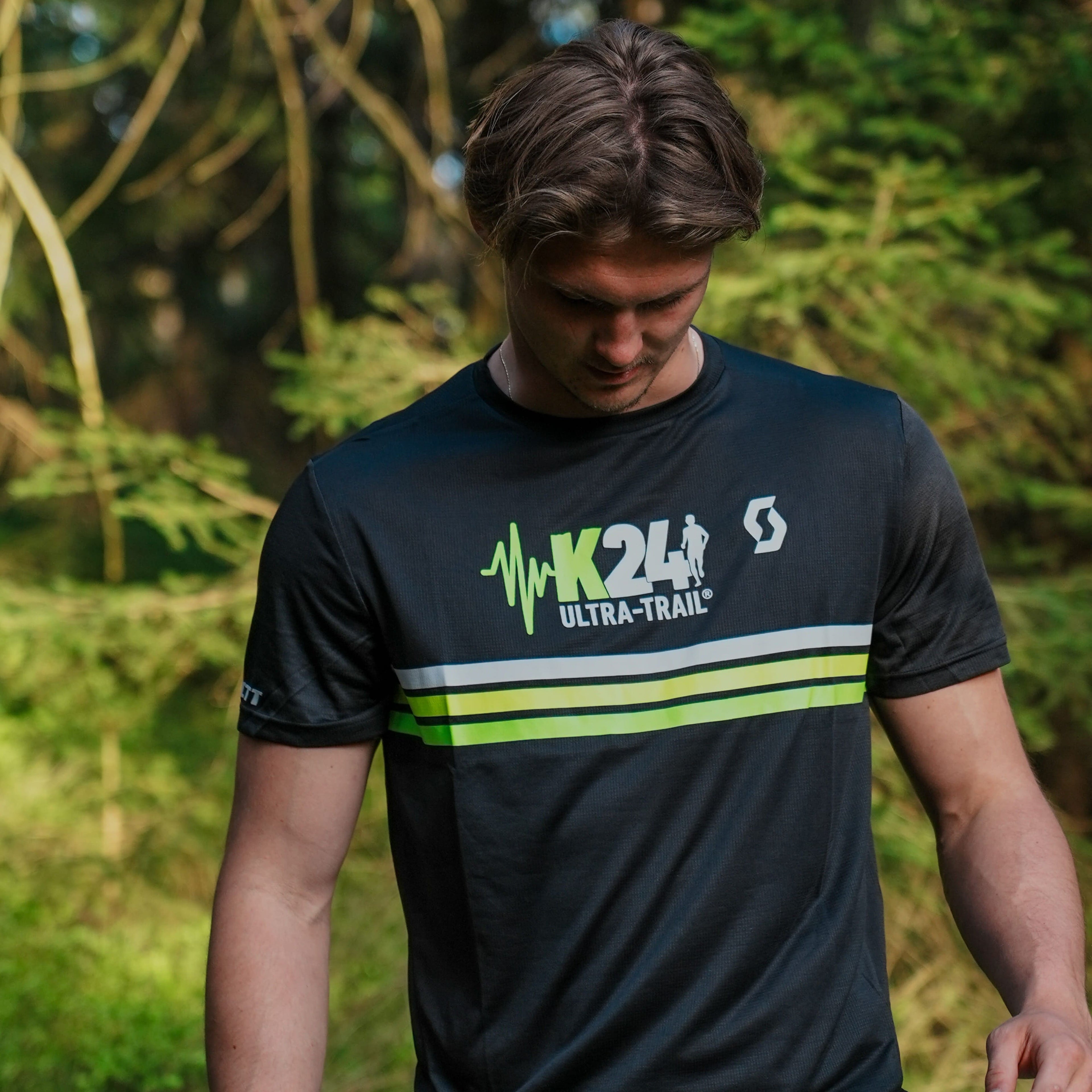 Person wearing a black athletic shirt with green and white design in a forest setting