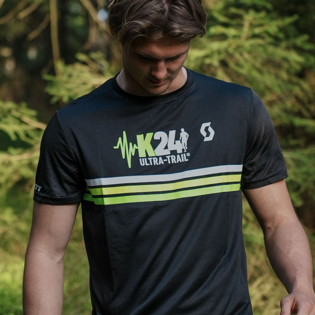 Person wearing a black t-shirt with green and white branding in a forest setting