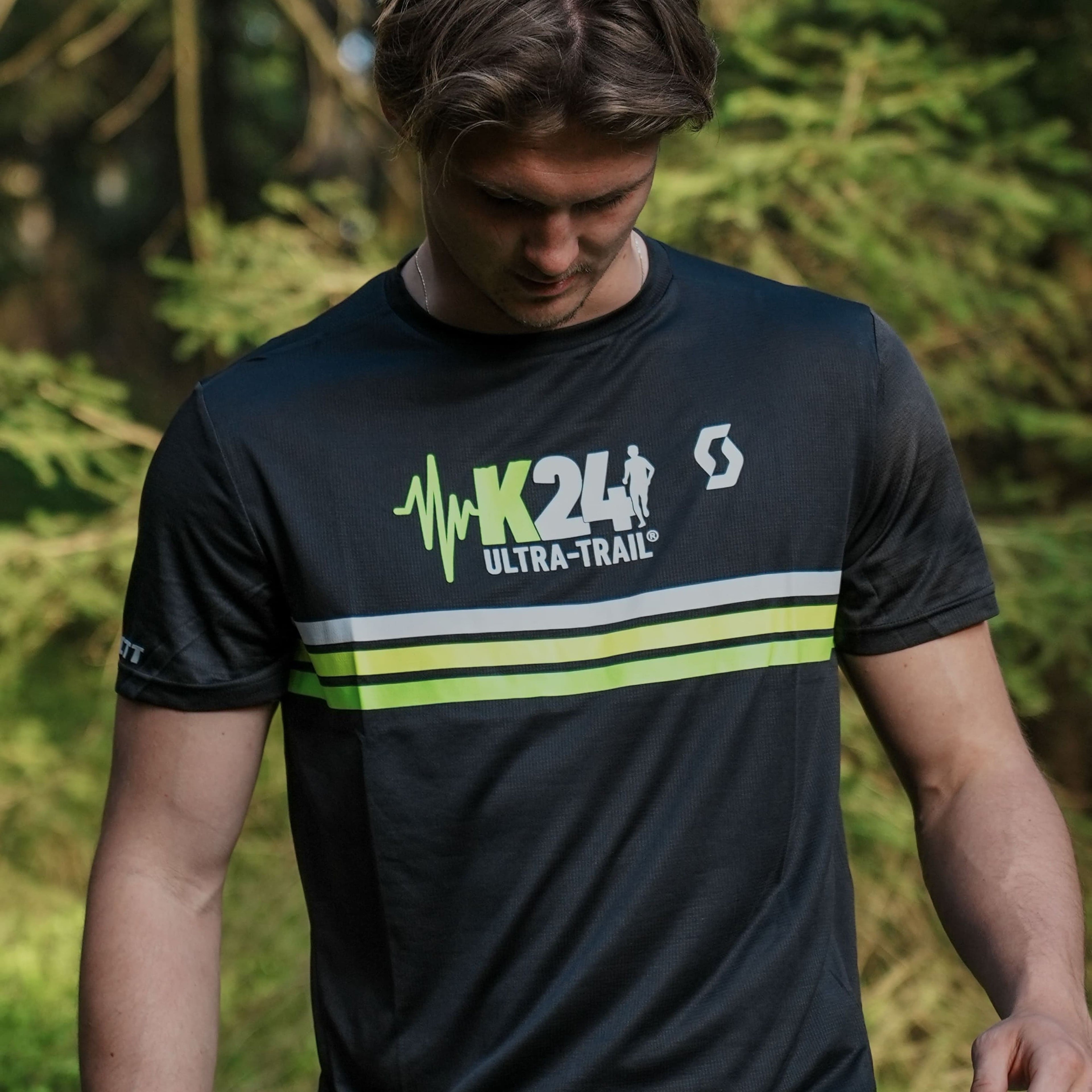 Person wearing a black t-shirt with green and white branding in a forest setting