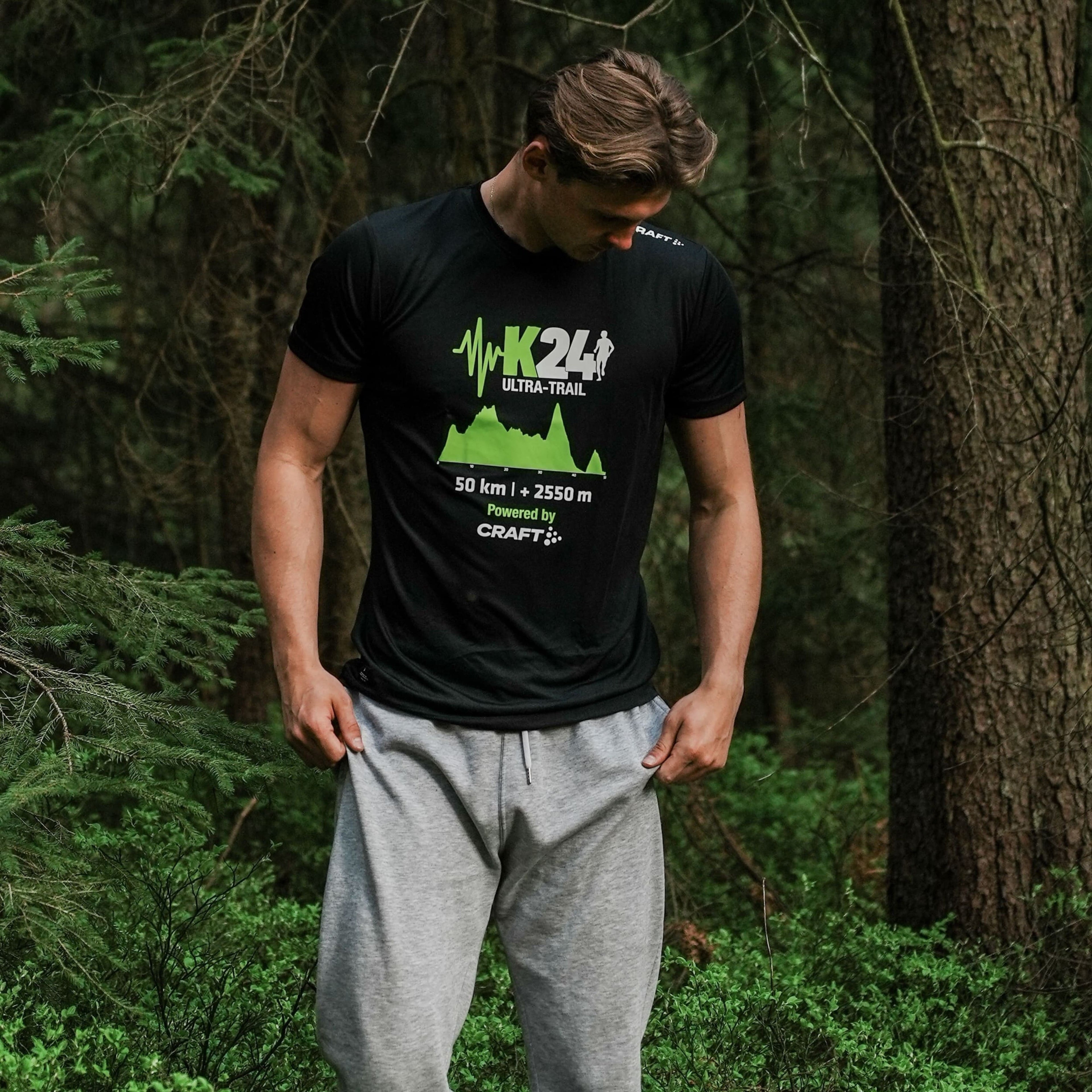 Person wearing a black t-shirt with green graphics and text in a forest setting