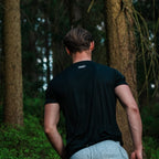 Person wearing a black t-shirt with text in a forest setting