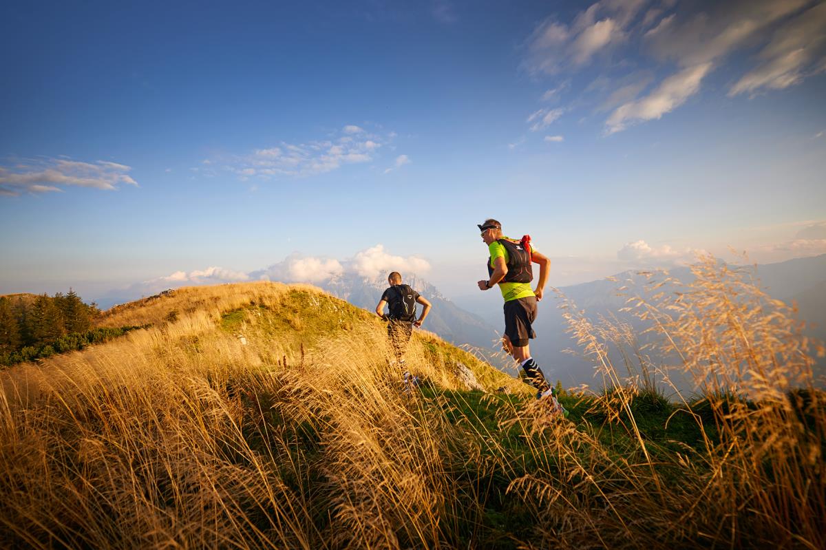 Two people running on a grassy hill with a clear blue sky