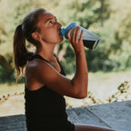 Woman drinking from a blue water bottle outdoors