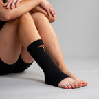 Person wearing black ankle sleeve with a brand logo on a gray background