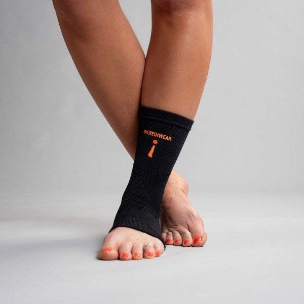 Black ankle support brace with orange branding on a neutral background