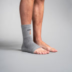 Person wearing a gray ankle support brace on a plain background