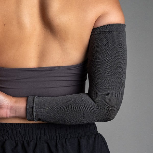 Person wearing a black compression sleeve on one arm against a gray background