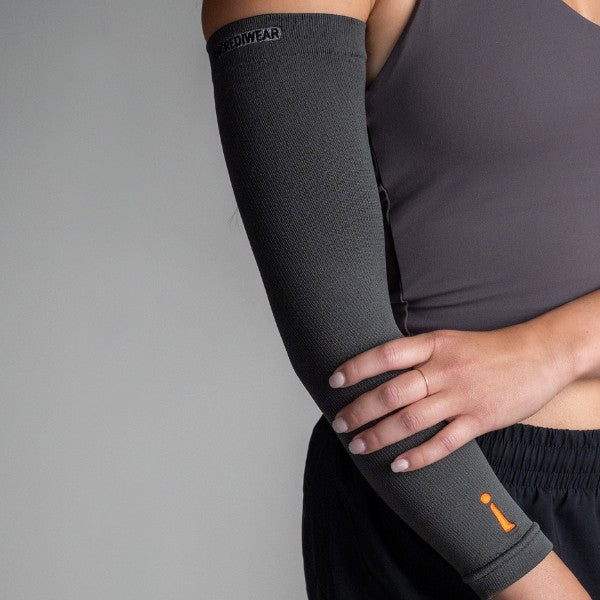 Person wearing a black compression arm sleeve with a visible brand logo on a gray background