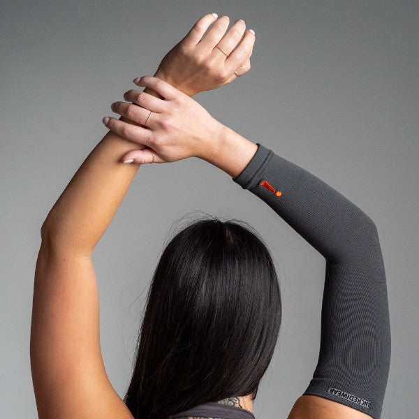 Person wearing a charcoal arm sleeve with a visible brand logo on a gray background