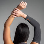 Person wearing a charcoal arm sleeve with a visible brand logo on a gray background