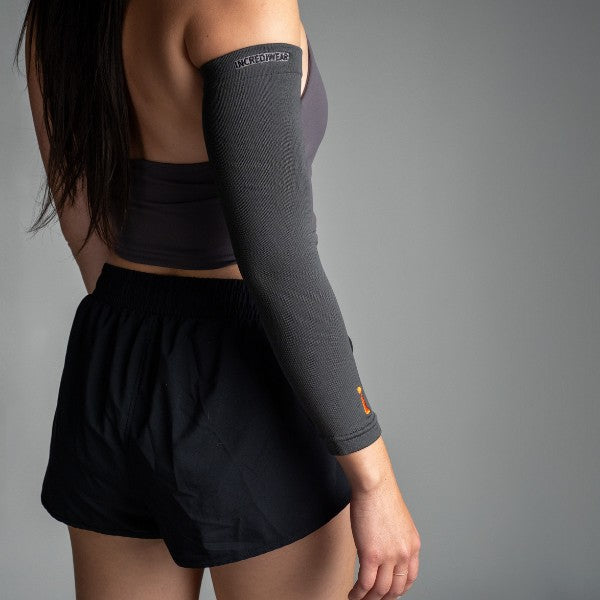 Person wearing a dark gray compression sleeve on one arm against a gray background