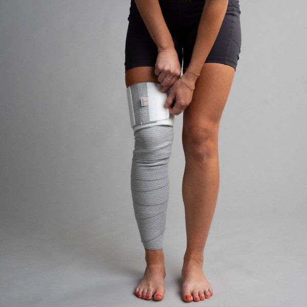 Person wearing a gray bandage tape  on one leg against a plain background