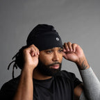 Man wearing a black beanie and black shirt against a gray background