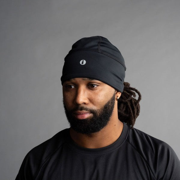 Man wearing a black beanie with a logo against a gray background