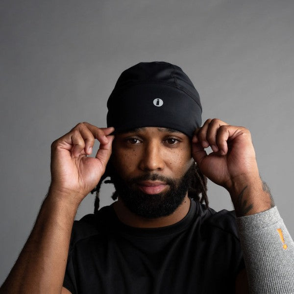 Man adjusting a black beanie against a gray background