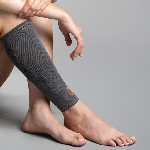 Person wearing a gray compression calf sleeve on their leg against a plain background