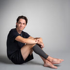 Man sitting on a gray background wearing a black shirt and gray compression calf sleeve on his leg.