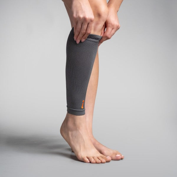 Person wearing a gray compression sleeve on their leg against a plain background