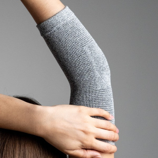 Gray compression sleeve on an elbow against a gray background