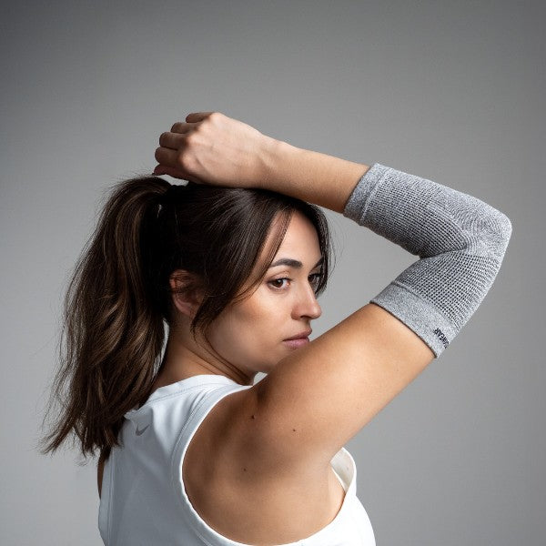 Woman wearing a gray arm elbow sleeve against a gray background