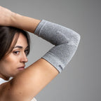 Woman wearing a gray elbow brace against a gray background