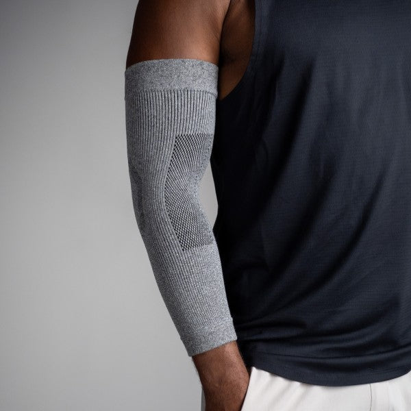 Person wearing a gray compression sleeve on their arm against a neutral background