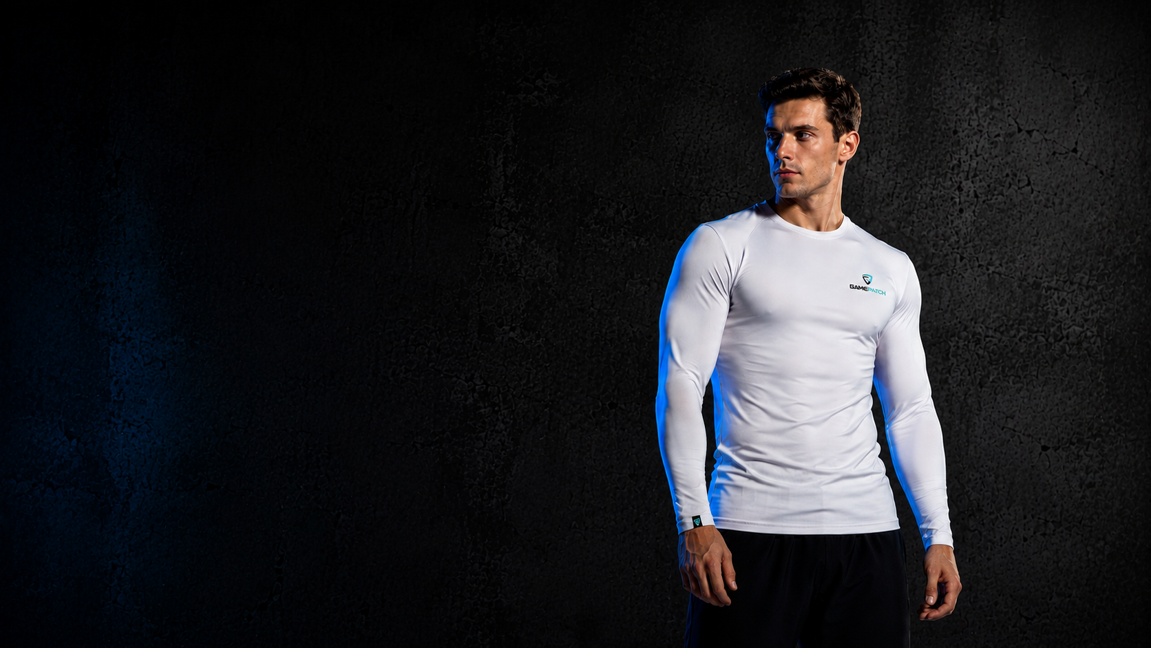 A man wearing a fitted white long-sleeve athletic compression shirt with a small green logo on the left chest, standing against a dark textured background.