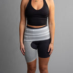 Person wearing a black sports bra and gray hip brace  on a gray background