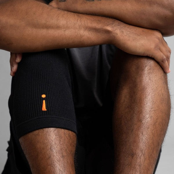 Person wearing black knee brace with a small orange logo on a gray background