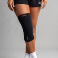 Black knee brace with orange branding on a gray background