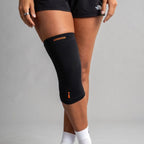 Black knee brace with orange branding on a gray background