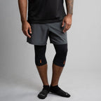 Person wearing gray athletic shorts and black knee brace on a plain background