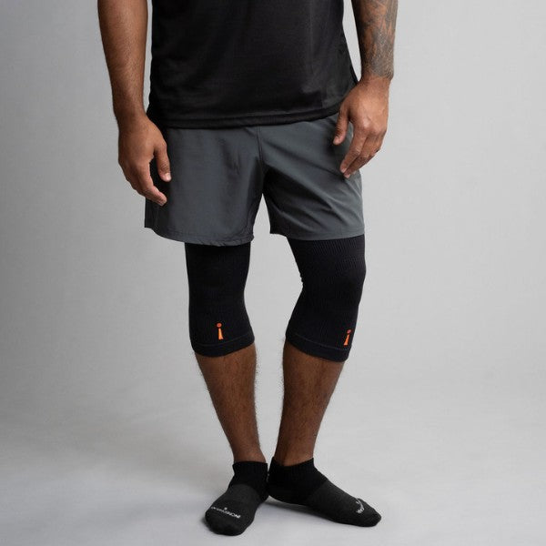 Person wearing gray athletic shorts and black knee brace on a plain background