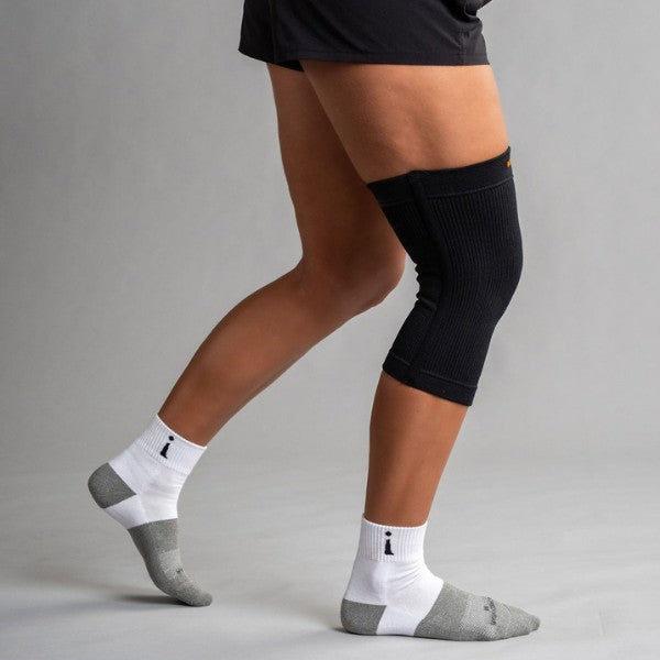 Person wearing black knee brace and white socks with gray toes on a plain background