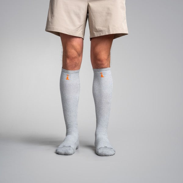 Person wearing gray knee-high socks with a small orange logo on a plain background