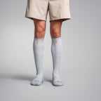 Person wearing gray knee-high socks with a small orange logo on a plain background